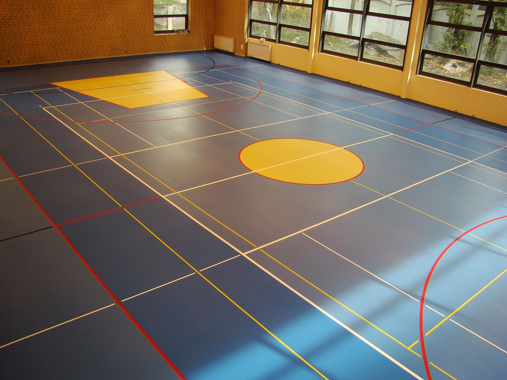 Niebieska poliuretanowa nawierzchnia sportowa w hali z żółtymi elementami i białymi, żółtymi oraz czerwonymi liniami wyznaczającymi pola gry, widok z góry.